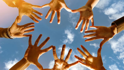 Acht Hände bilden einen Kreis vor blauem Himmel