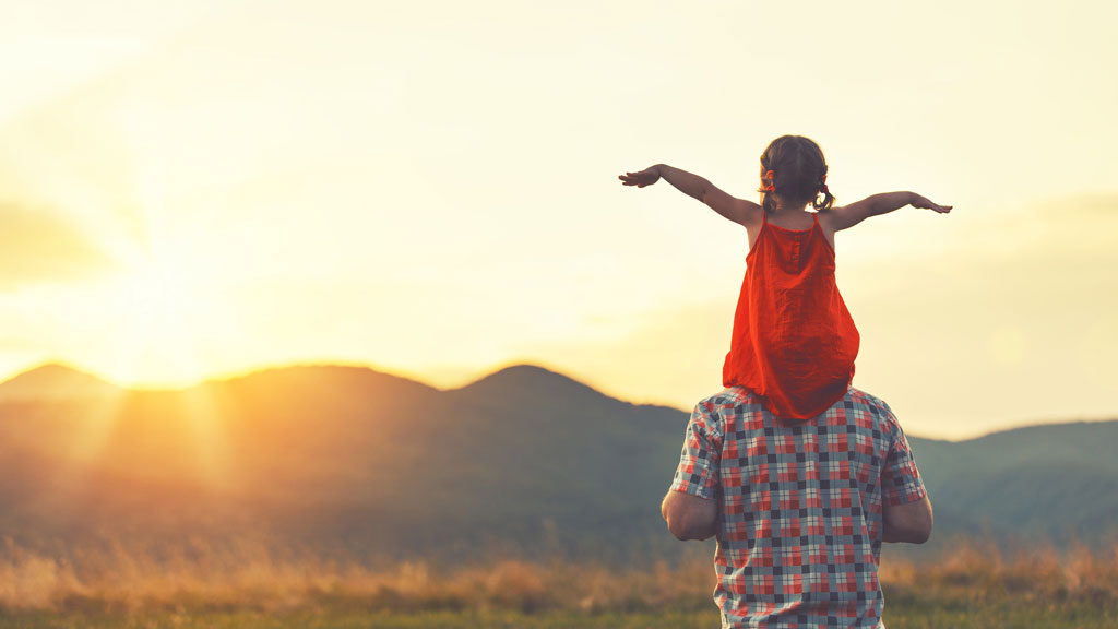 Vater mit kleiner Tochter auf Schultern bei Sonnenaufgang in Bergen