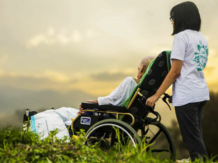 Pflegerin schiebt alten Menschen im Rollstuhl