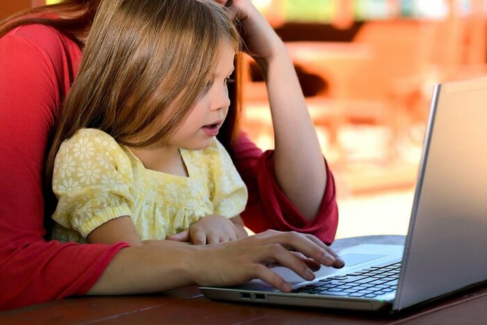 Kleines Mädchen sitzt mit Mama vor Laptop