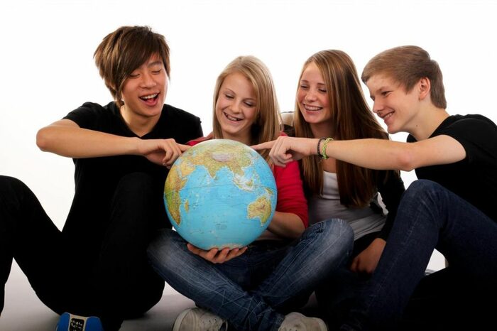 Vier Jugendliche am Boden sitzend halten Erdkugel in der Hand