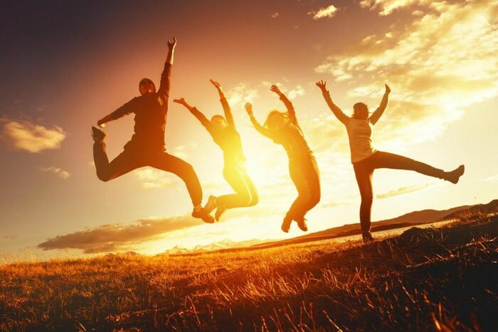 Vier Jugendliche auf Wiese bei Sonnenuntergang, springen in die Luft