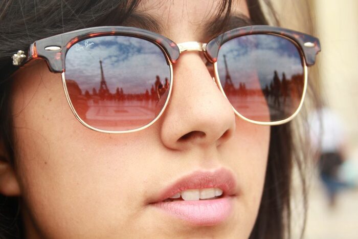 Junge Frau mit Sonnenbrille, in der sich der Eiffelturm spiegelt